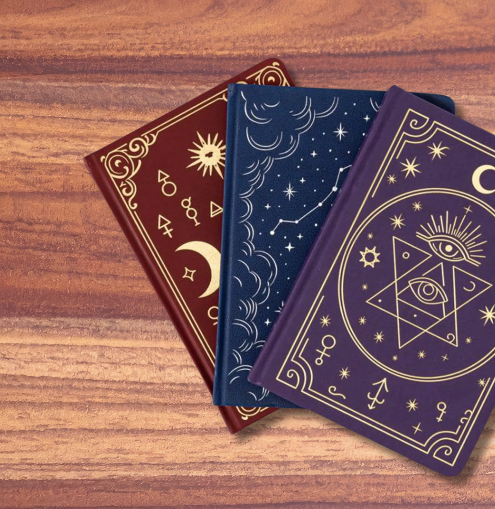 Three tarot card decks with ornate celestial and mystical designs, arranged diagonally on a wooden surface against a solid pink background.