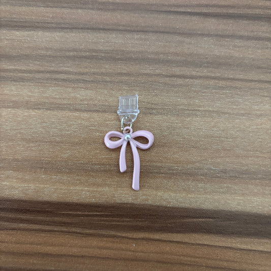 A small pink bow-shaped charm with a clear plastic clip, placed on a brown wooden surface.