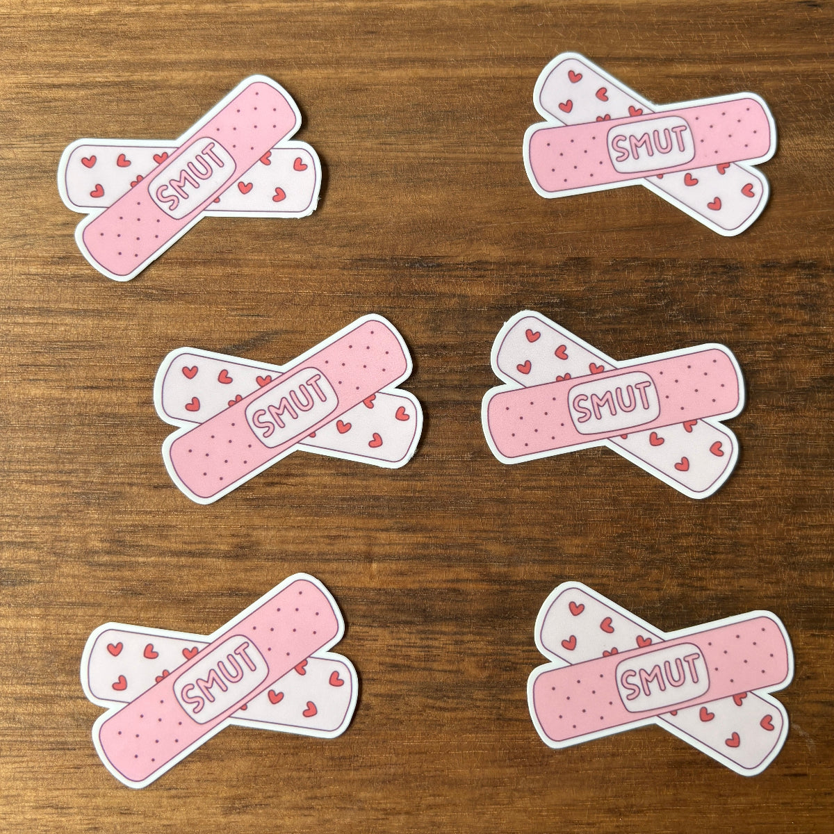 Pink and white bandage-like stickers with 'SMUT' text on a wooden surface