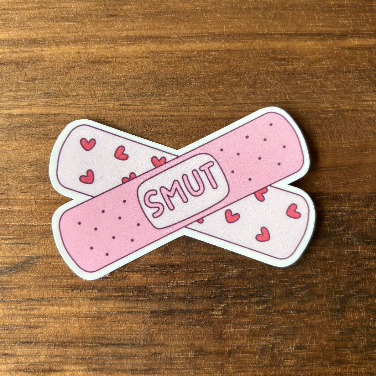 Pink bandage stickers with 'SMUT' text and heart patterns on a wooden surface