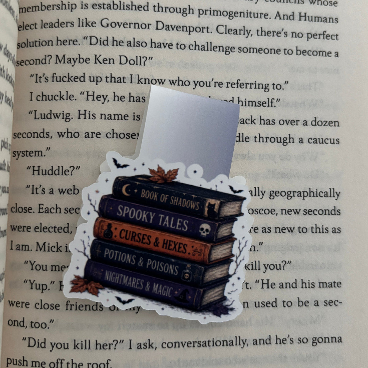 A decorative magnetic bookmark styled like a stack of spooky books with the title 'Spooky Tales' and other themed titles, placed on top of an open book page.