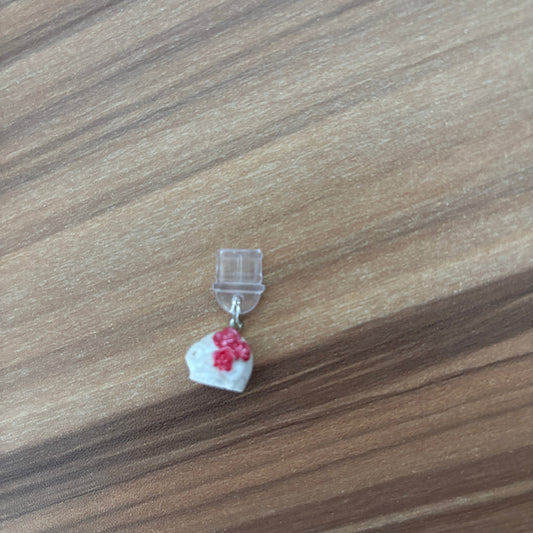 A miniature clear plastic clip with a small white skull and red cherry blossom charm, placed on a brown wood-grain surface.